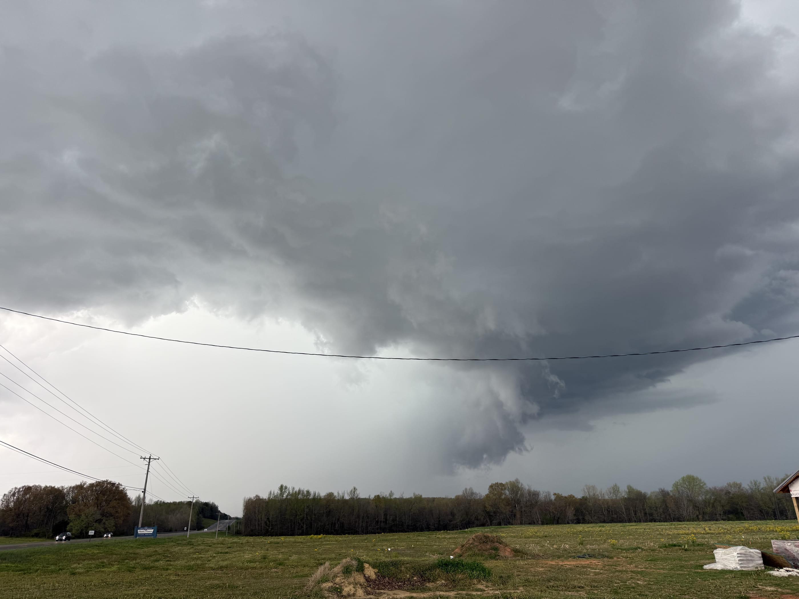 A wall cloud beyond a treeline, framed by power lines crossing the foreground.