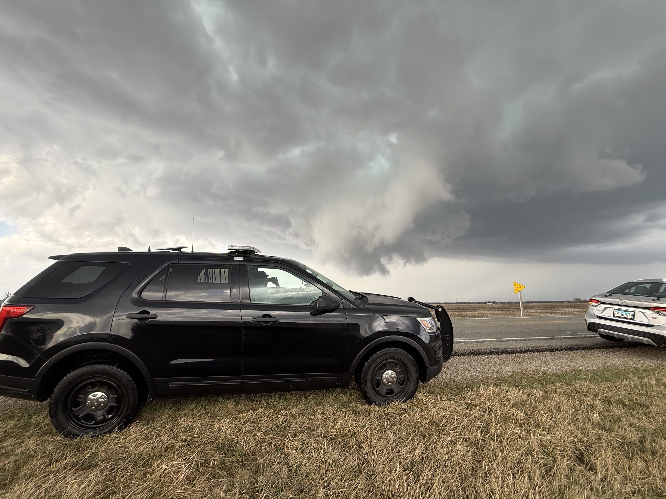 The TwistedWX chase vehicle parked on a grass shoulder with a lowering storm base behind it.