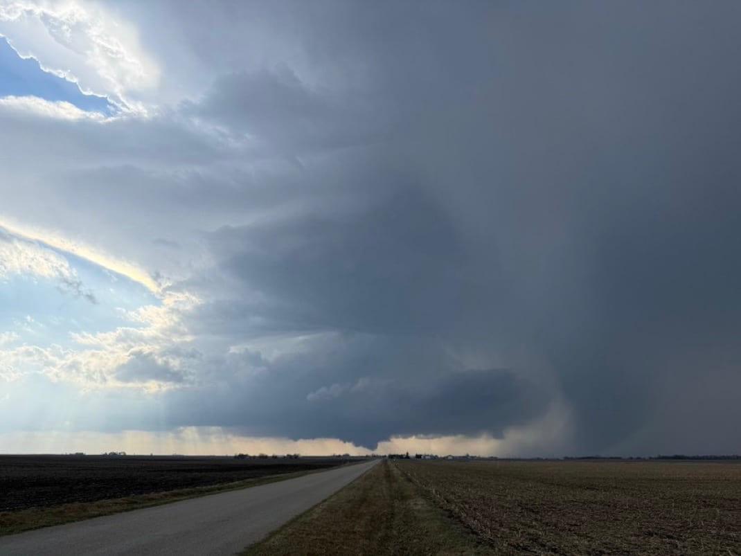 A country road running straight toward a rain core, with clearing sky to the west.