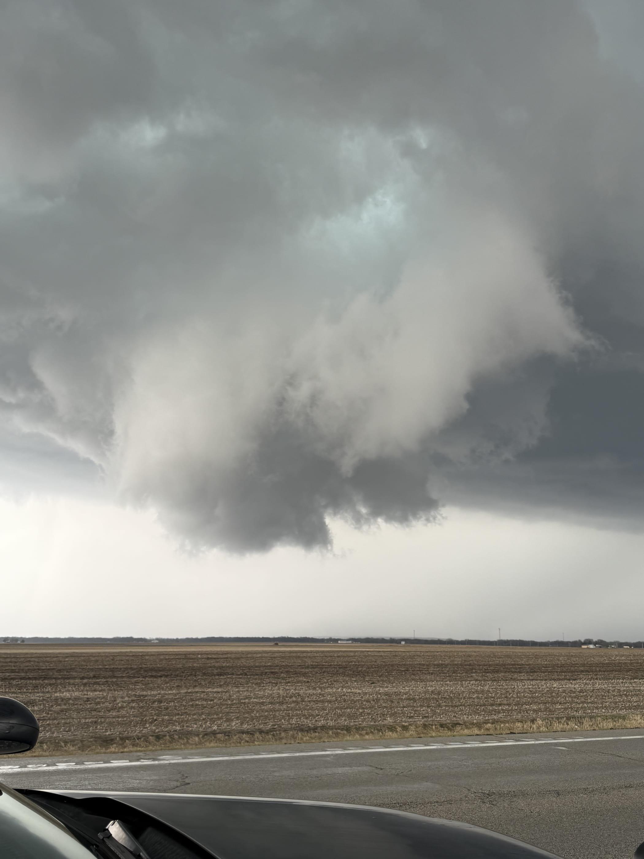Vertical framing of a wall cloud and rain-free base above open farmland, shot over the hood of the chase vehicle.